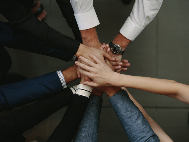 A group of people in a circle, with their hands stacked in the middle.
